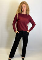 Woman wearing a burgundy sweater and black pants against a plain background