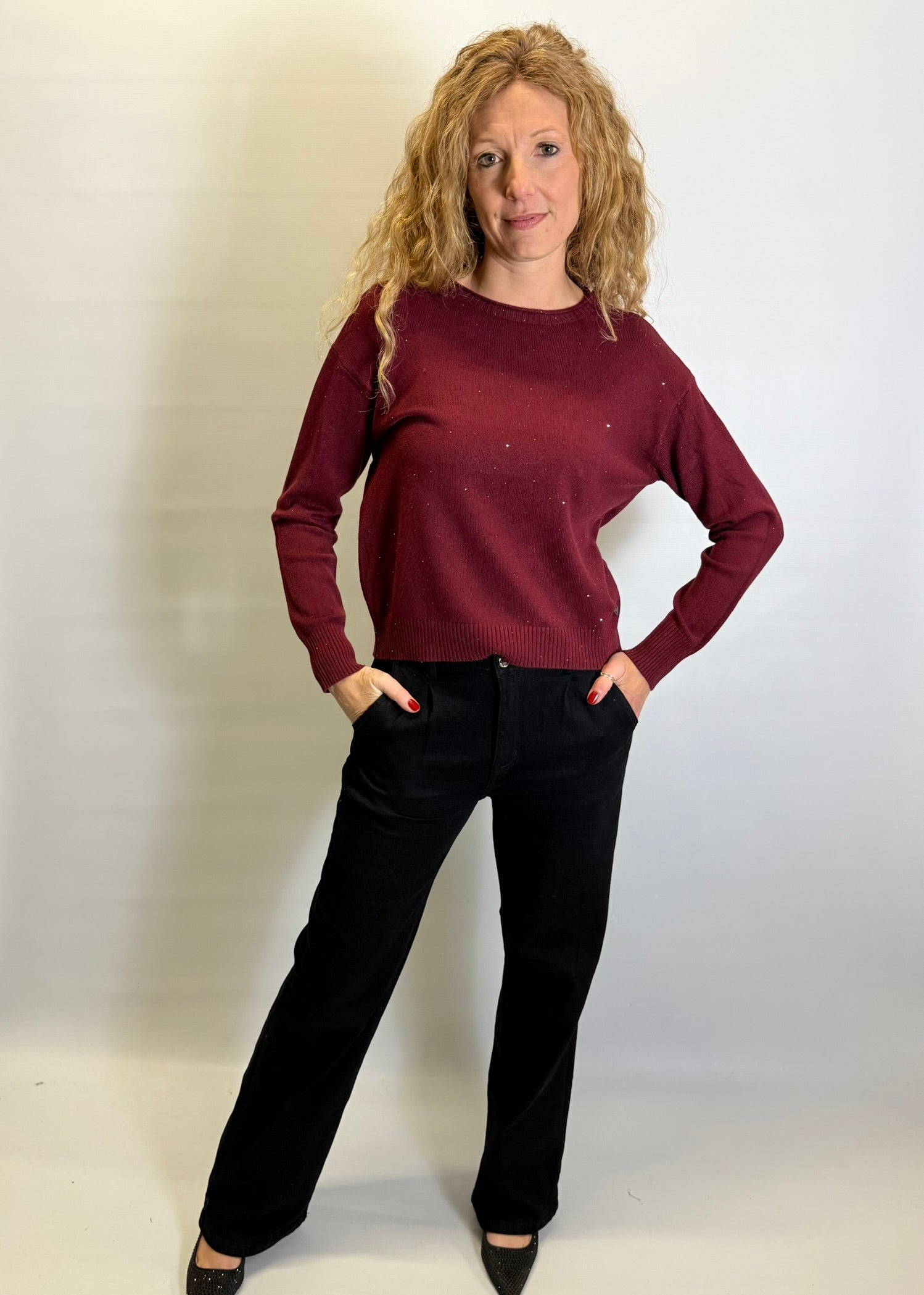 Woman wearing a burgundy sweater and black pants against a plain background