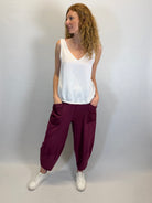 Woman wearing a white sleeveless top and maroon pants against a plain background