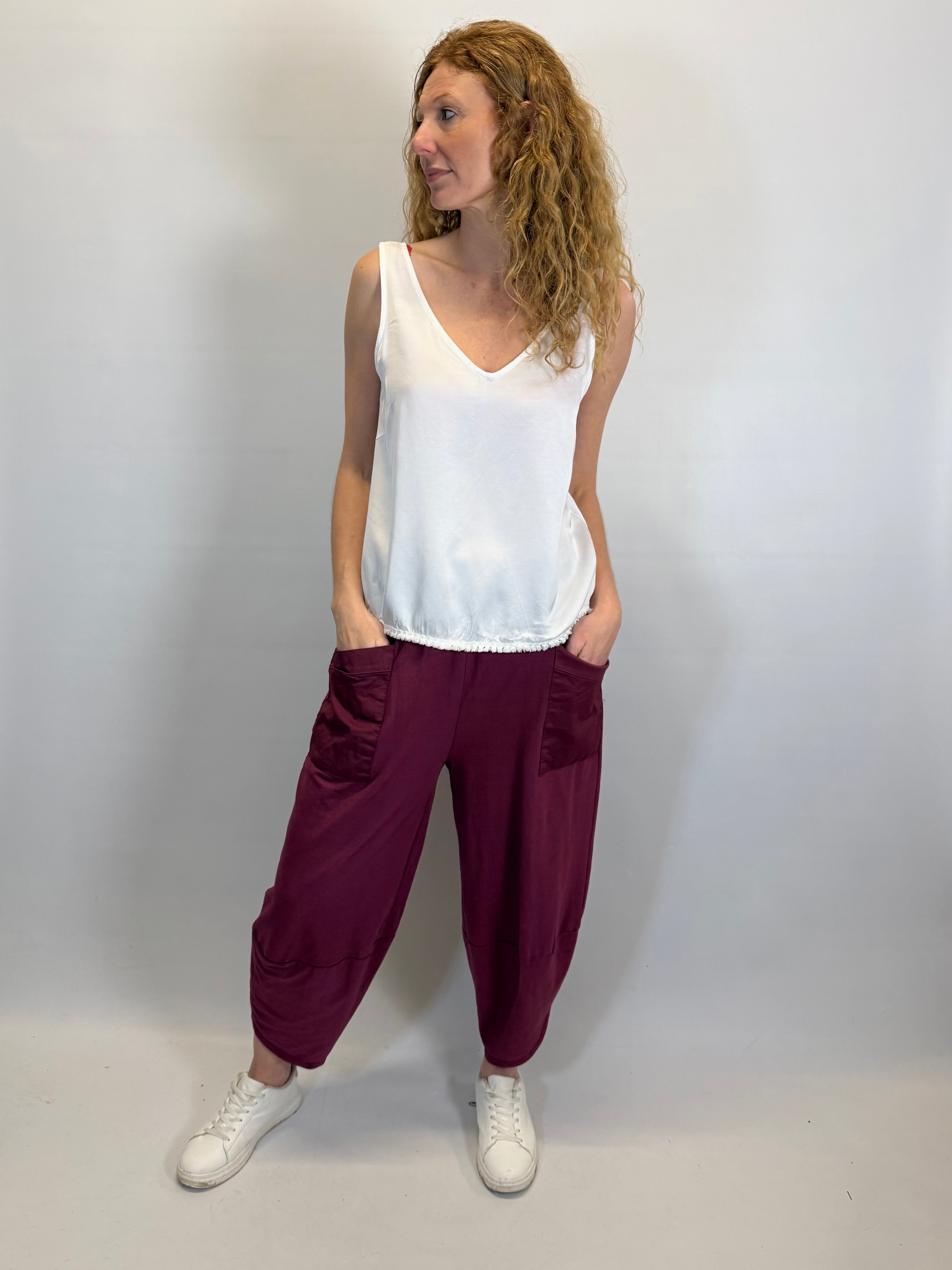 Woman wearing a white sleeveless top and maroon pants against a plain background