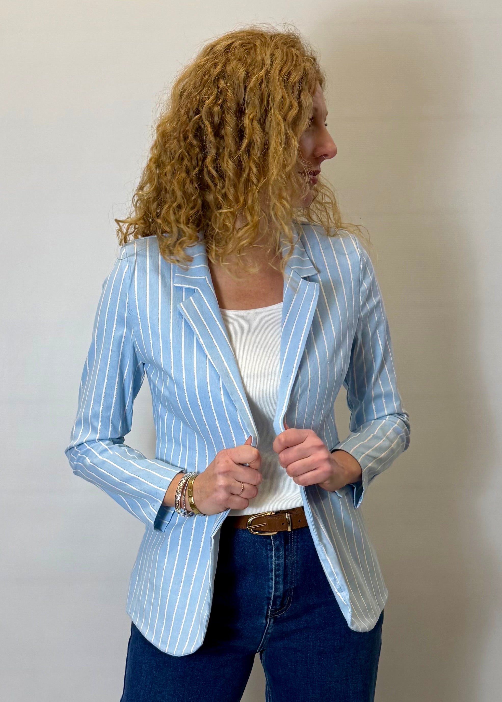 Woman wearing a light blue striped blazer over a white top and blue jeans against a plain background