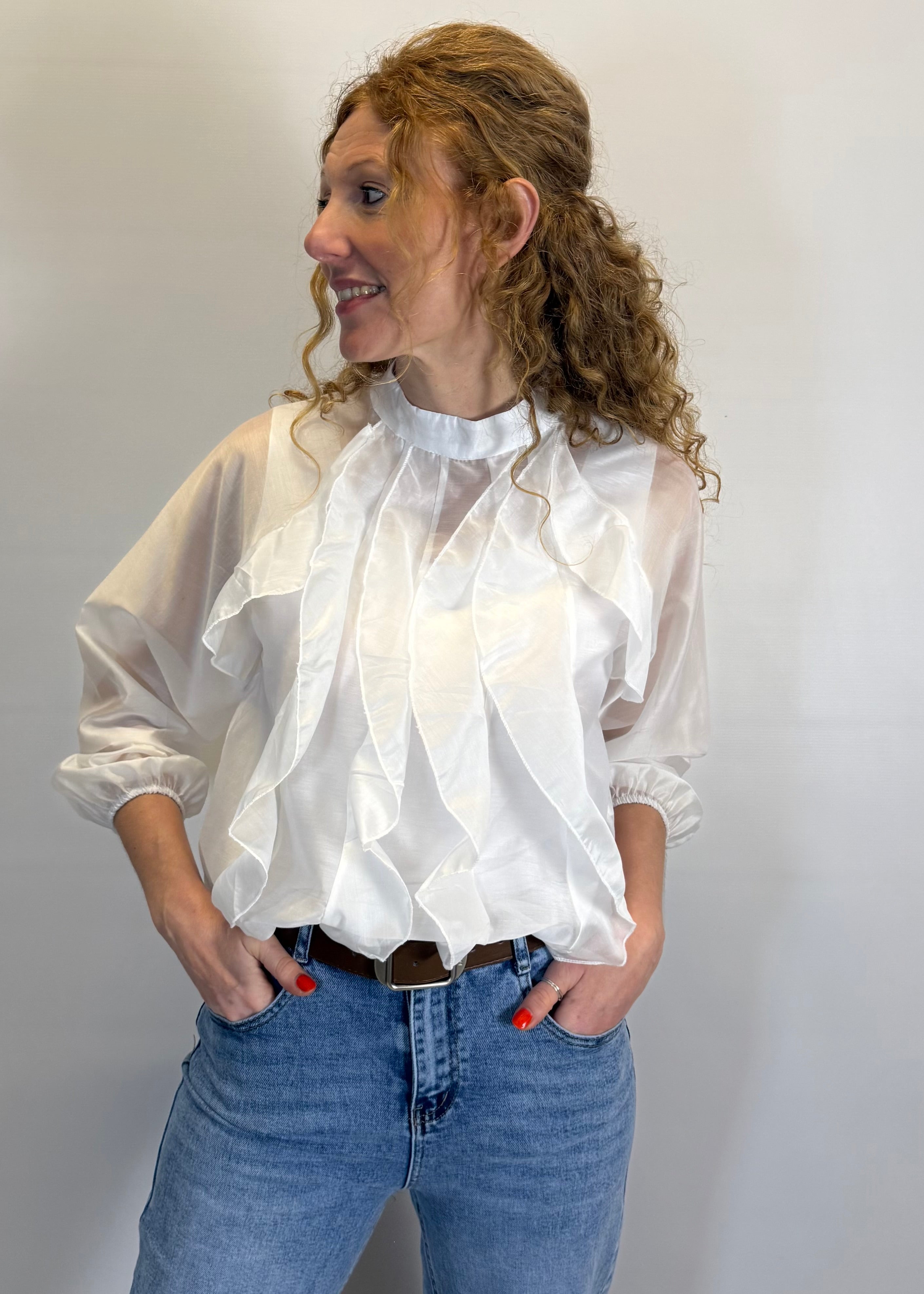 Woman wearing a white blouse with ruffled details and blue jeans against a plain background
