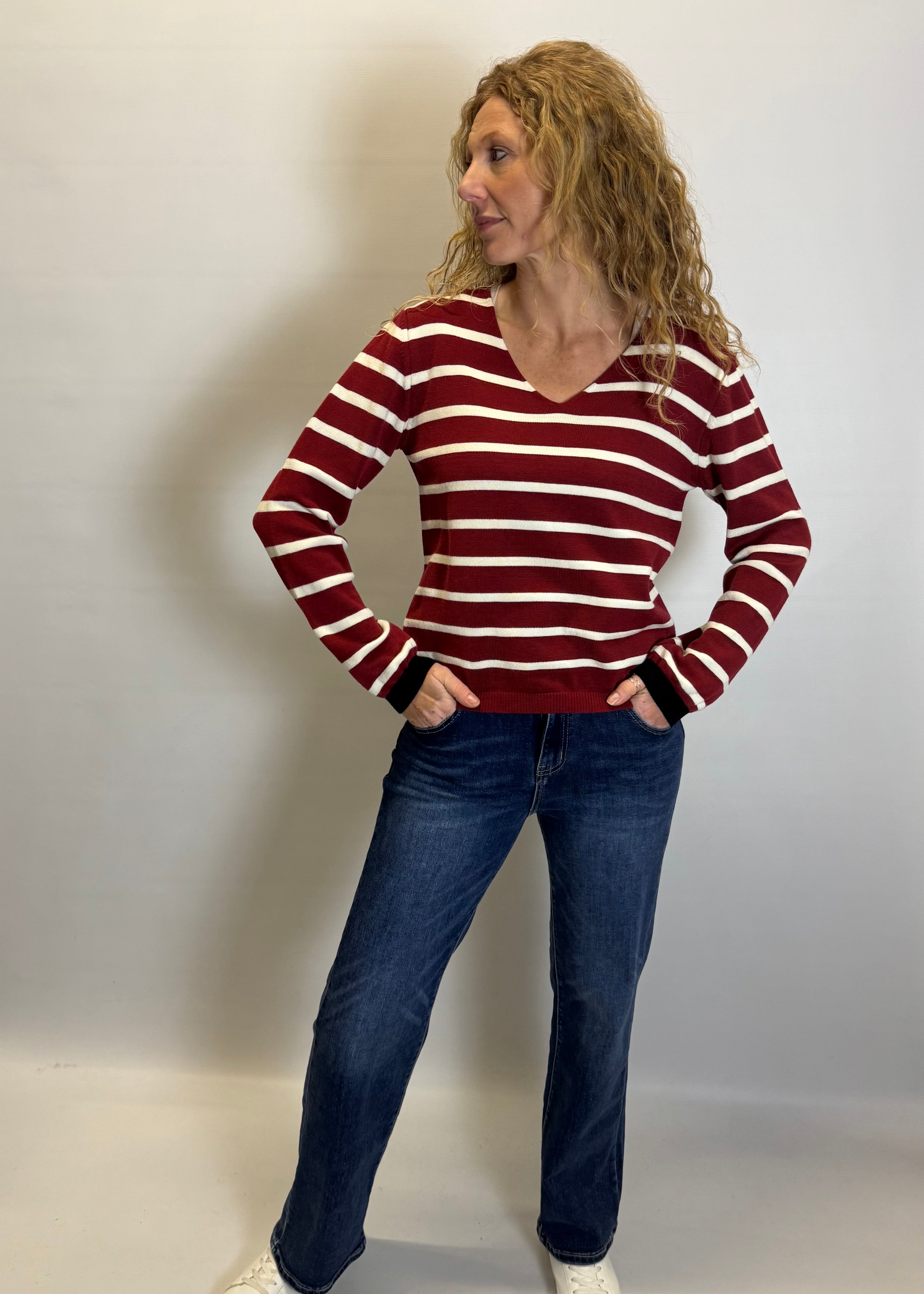 Woman wearing a red and white striped sweater and blue jeans against a plain background