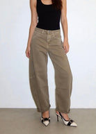 A model wearing a pair of wide-leg, cuffed khaki cargo pants, styled with a black tank top and black-and-white pointed-toe heels against a plain white wall.