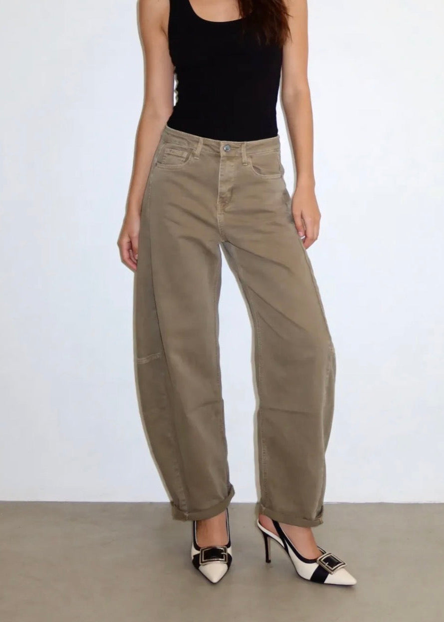 A model wearing a pair of wide-leg, cuffed khaki cargo pants, styled with a black tank top and black-and-white pointed-toe heels against a plain white wall.