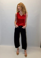 Woman wearing a red sleeveless top and black pants against a plain background
