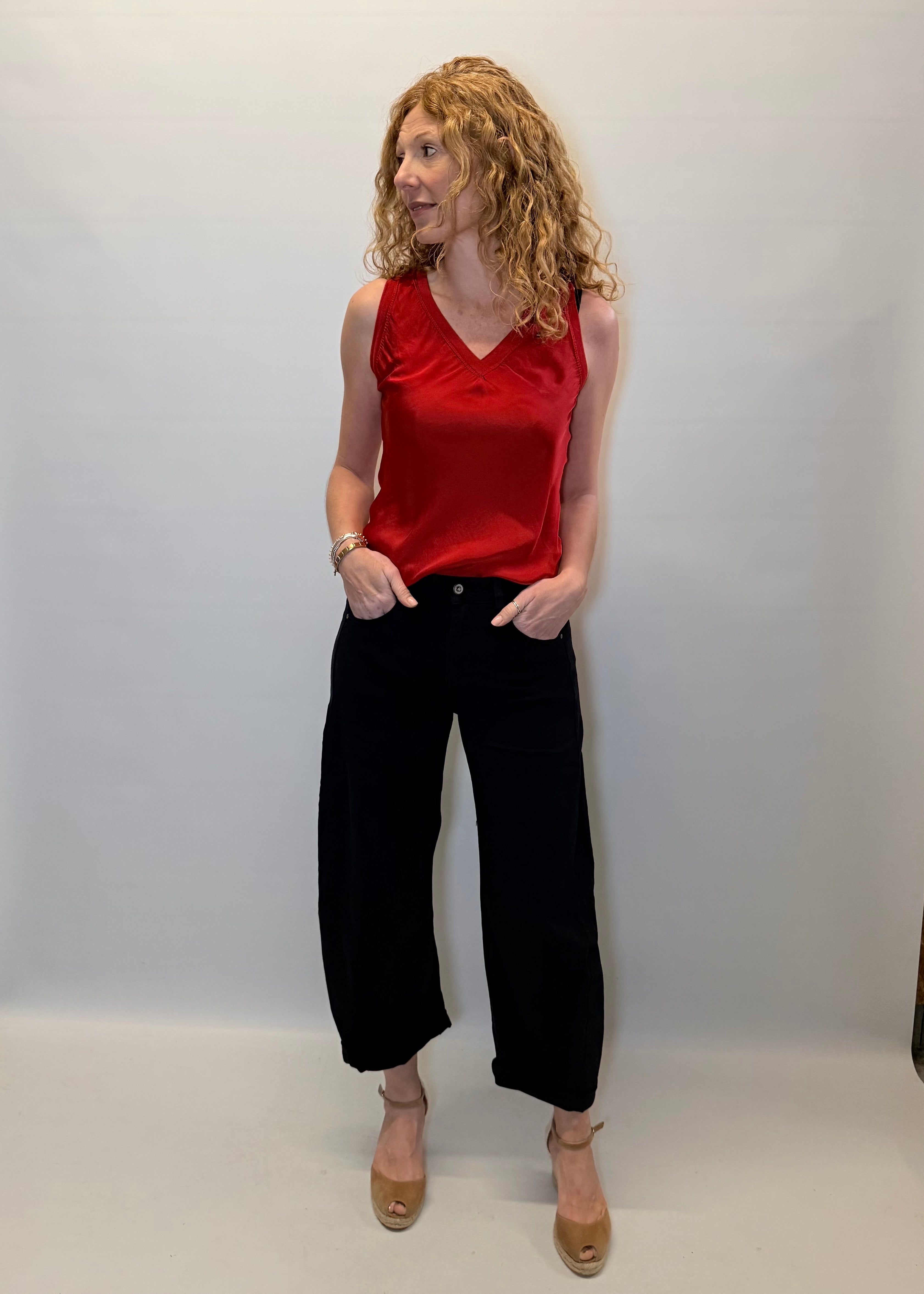 Woman wearing a red sleeveless top and black pants against a plain background