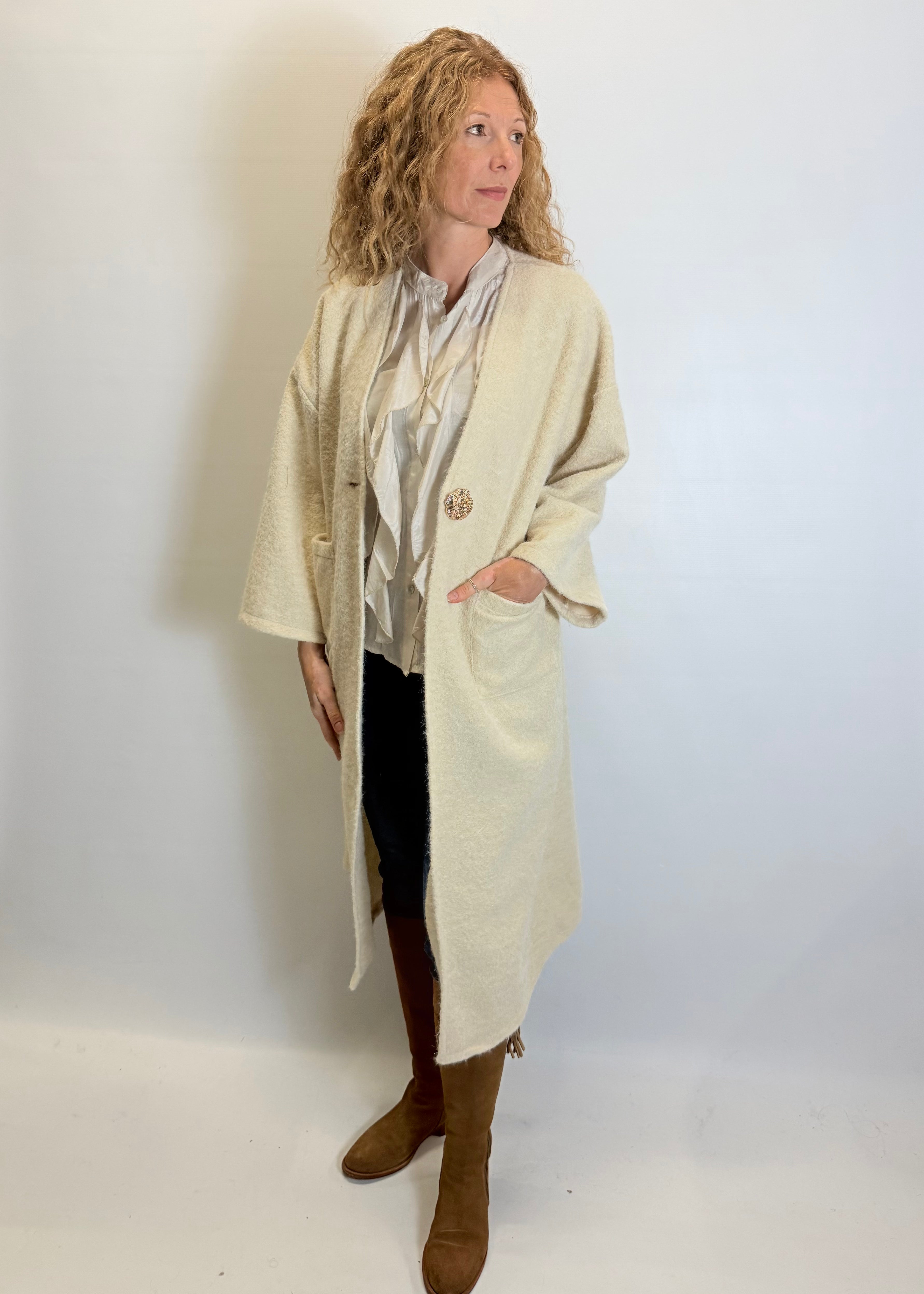 Woman wearing a long beige coat over a patterned top with a plain background