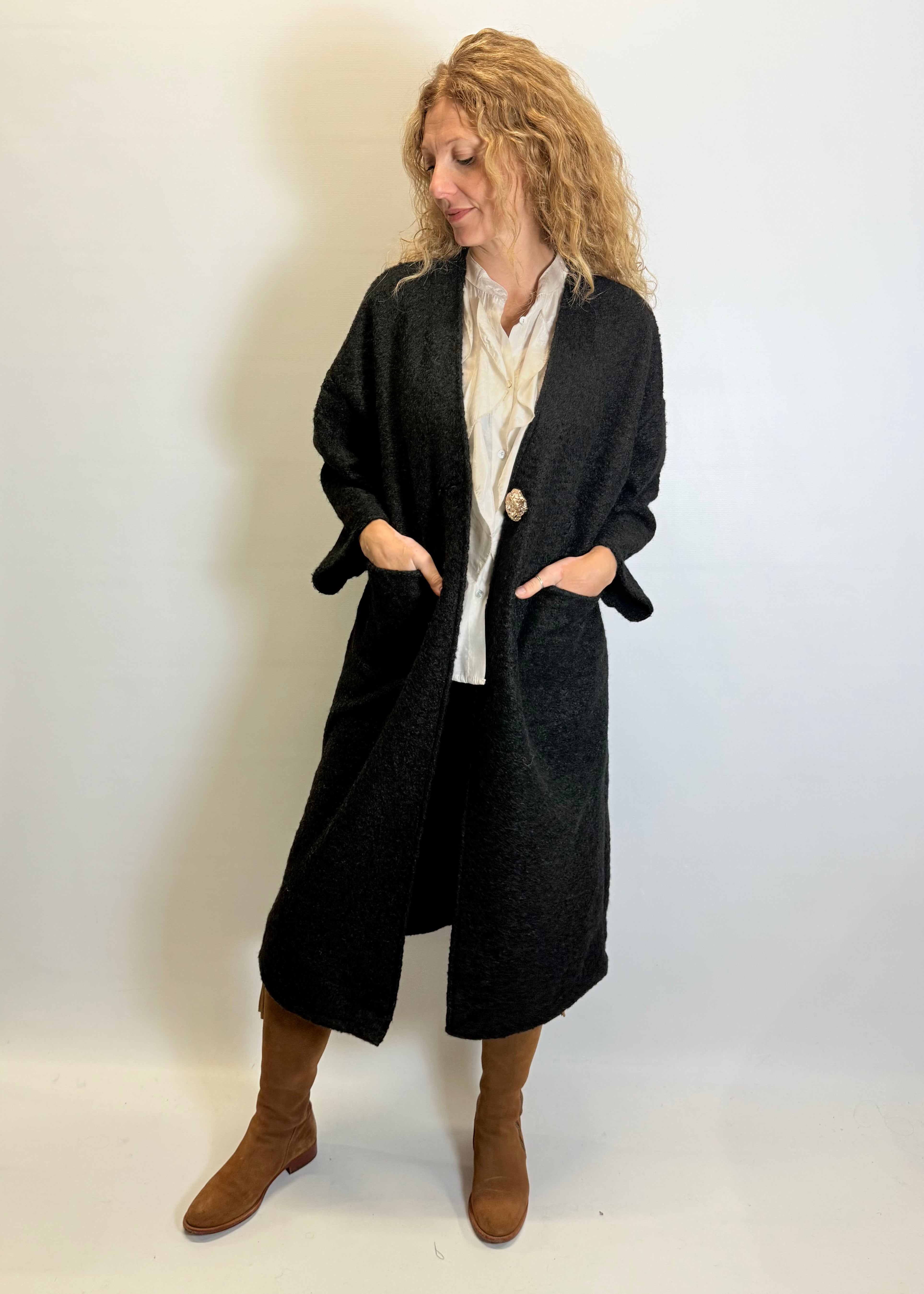 Woman wearing a long black coat over a white shirt on a plain background