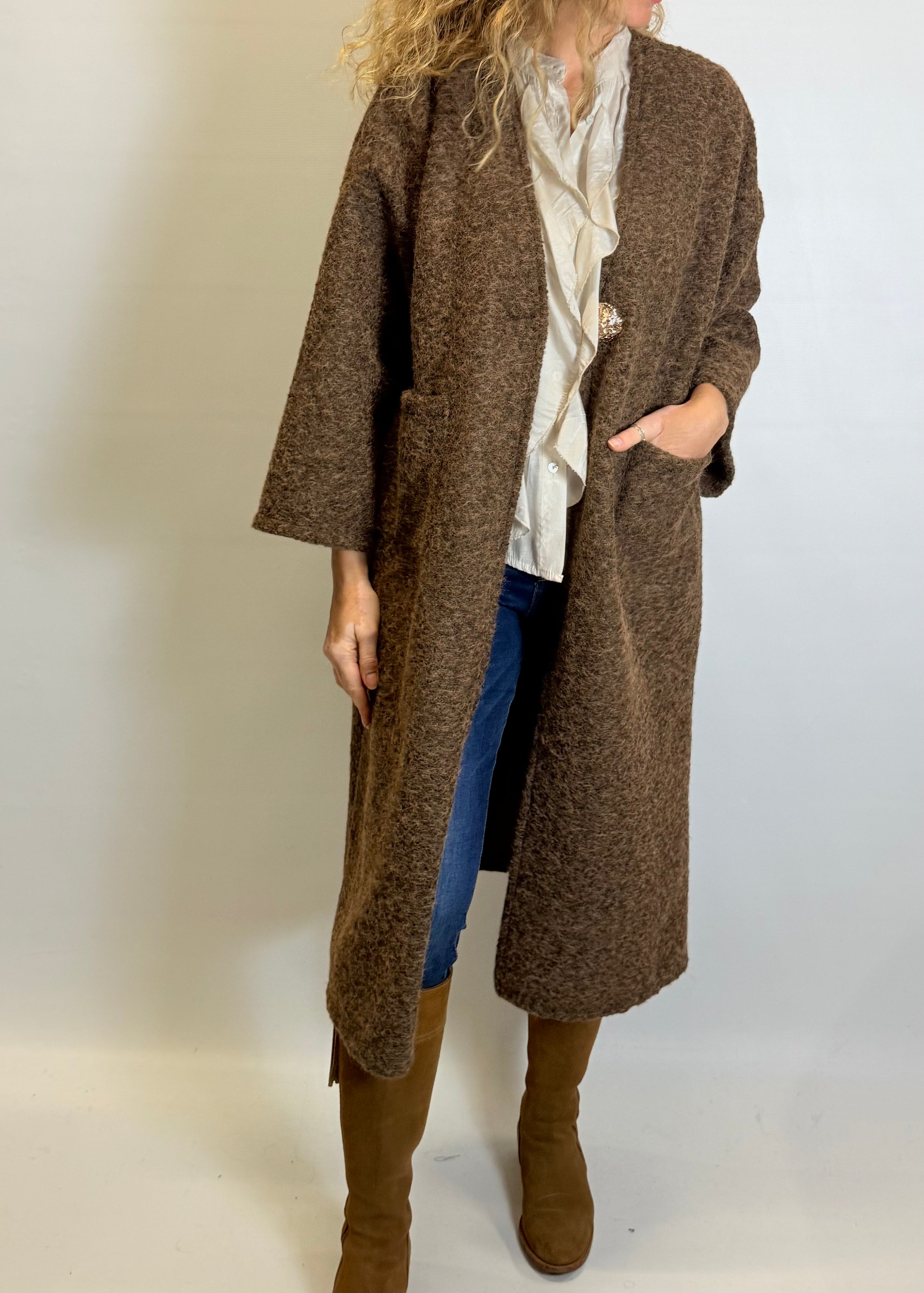 Person wearing a long brown coat with a plain background