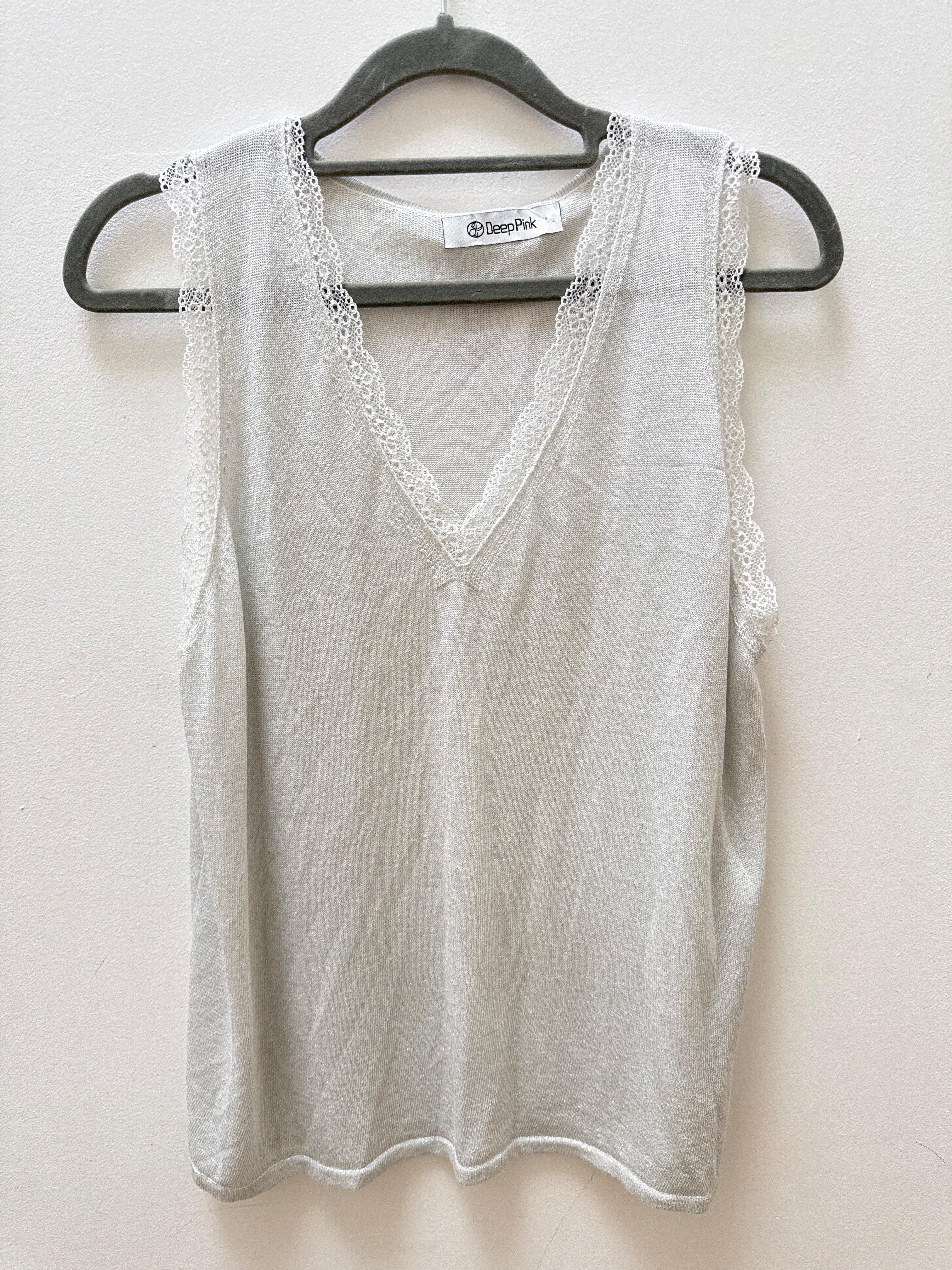A light gray sleeveless V-neck top with delicate lace trim along the armholes and neckline, hanging on a black hanger against a plain off-white wall.