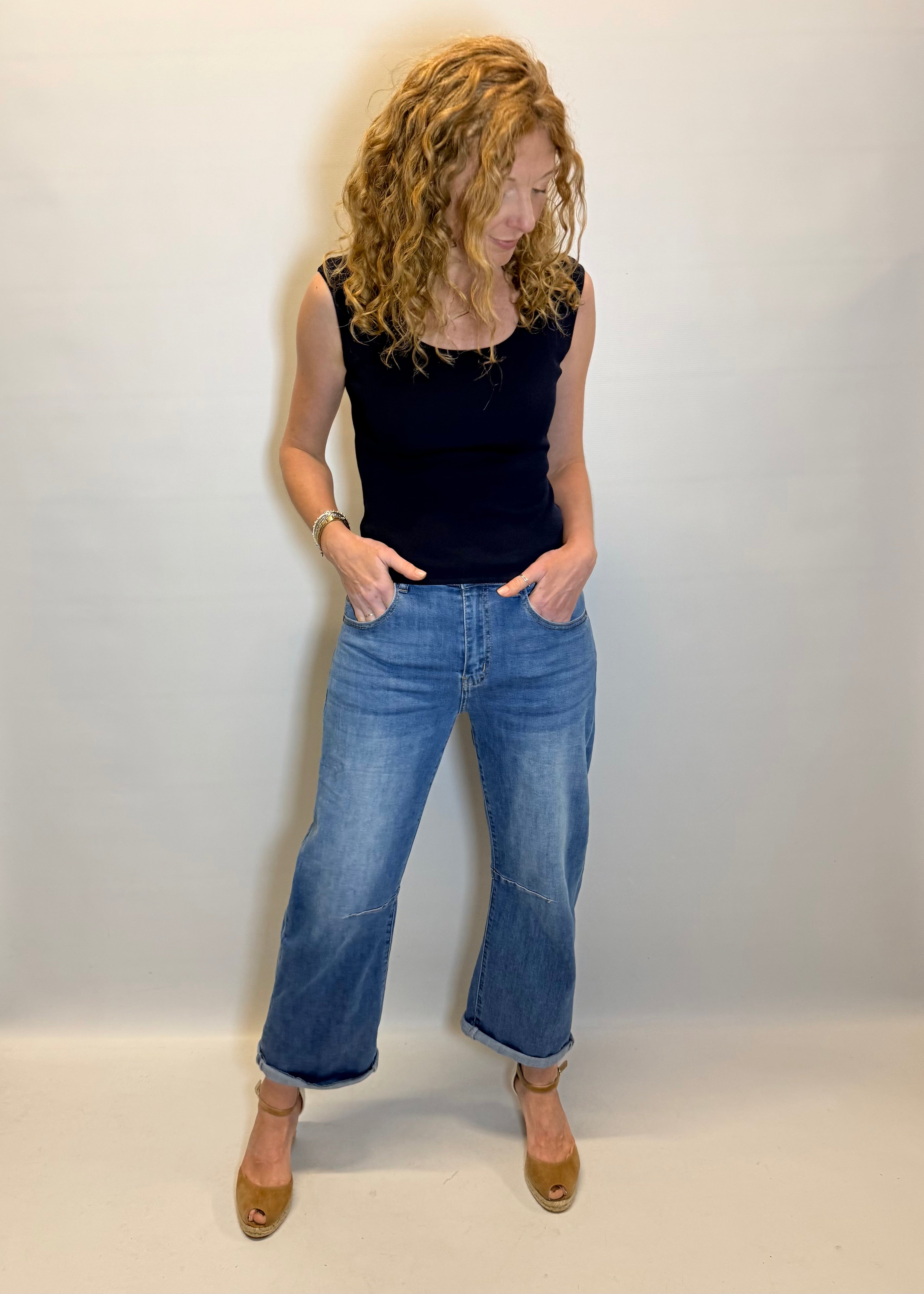 Woman wearing a black top and blue jeans against a white background