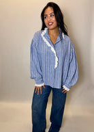 Woman wearing a blue and white striped shirt with lace trim and jeans against a beige background