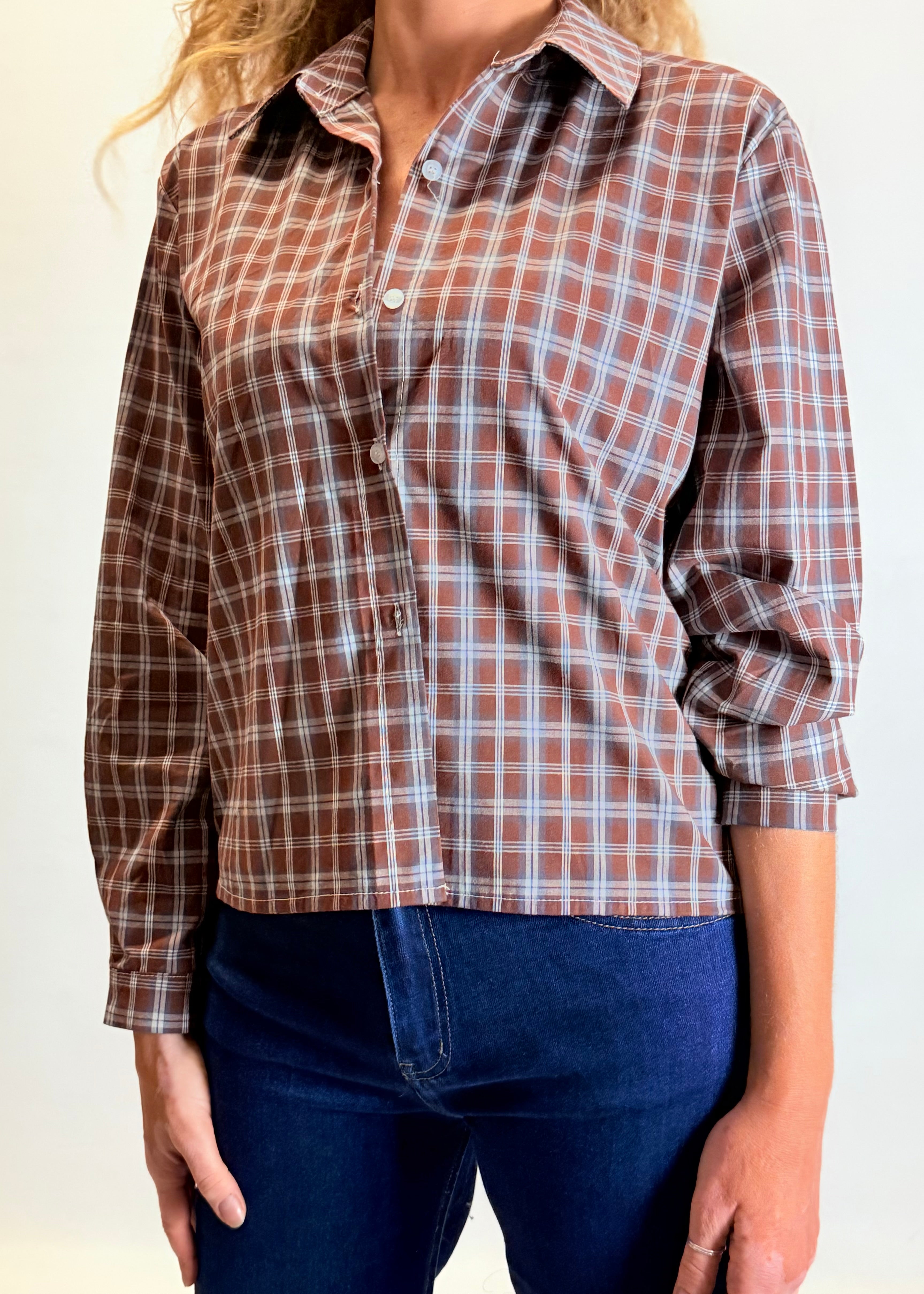 Person wearing a brown plaid shirt and blue jeans on a plain background