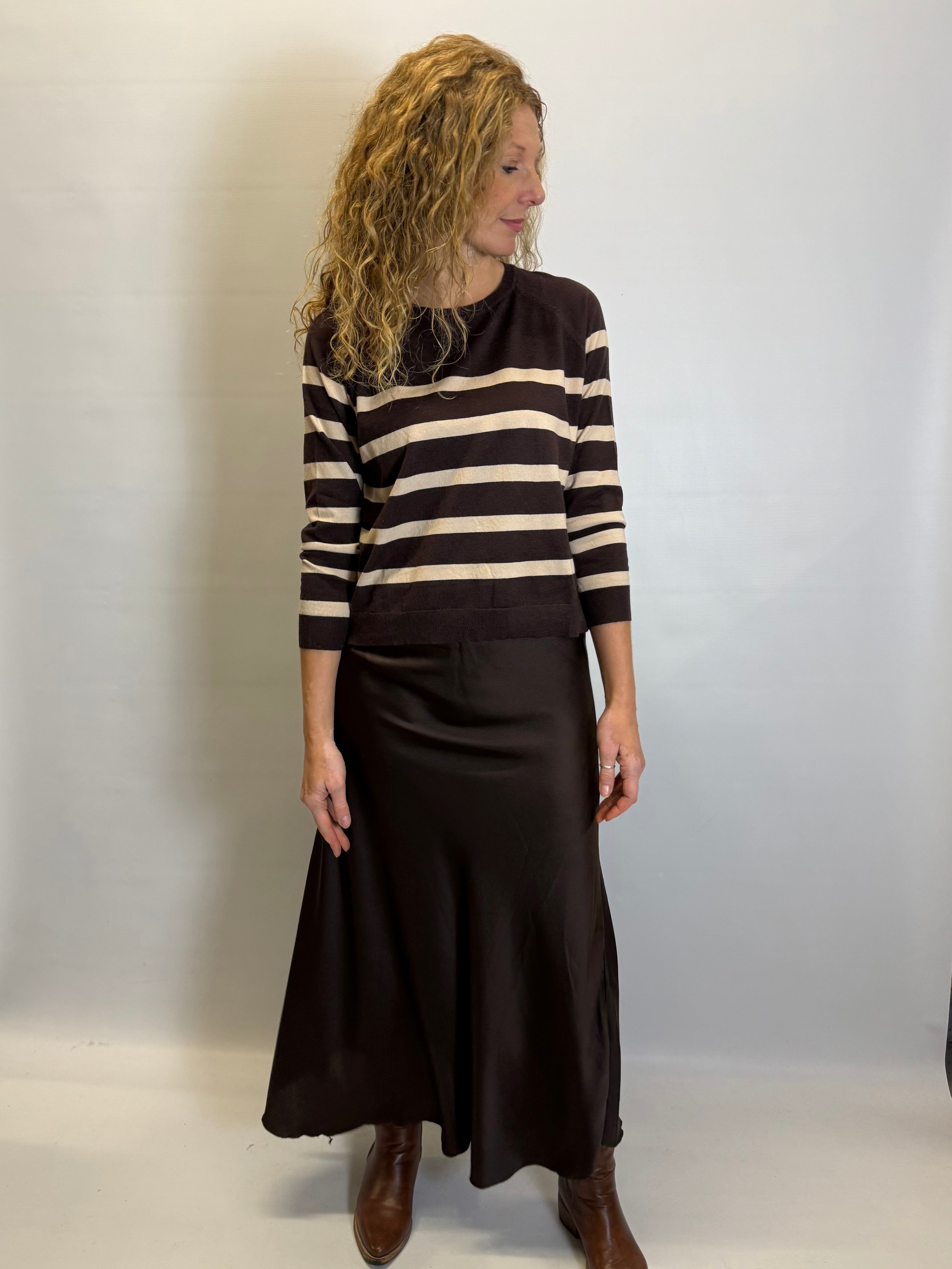 Woman wearing a black and beige striped sweater with a black skirt against a white background