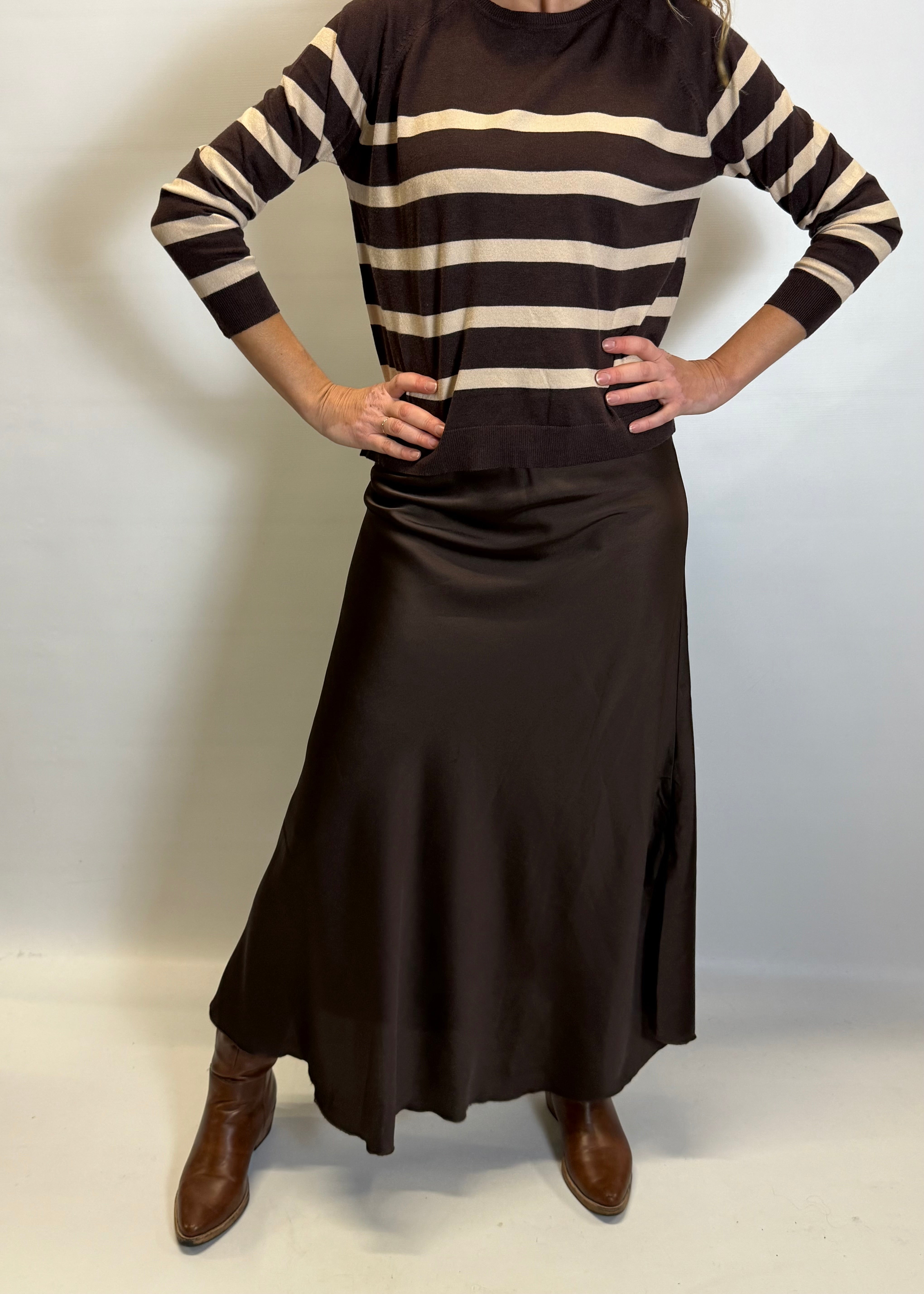 Person wearing a brown and beige striped sweater with a long brown skirt on a white background