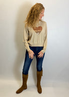Woman wearing a beige sweater with a heart design, blue jeans, and brown boots against a white background