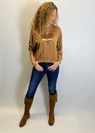 Woman wearing a brown sweater with a heart design, blue jeans, and brown knee-high boots against a white background.