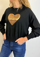 Person wearing a black sweatshirt with a gold sequin heart design.