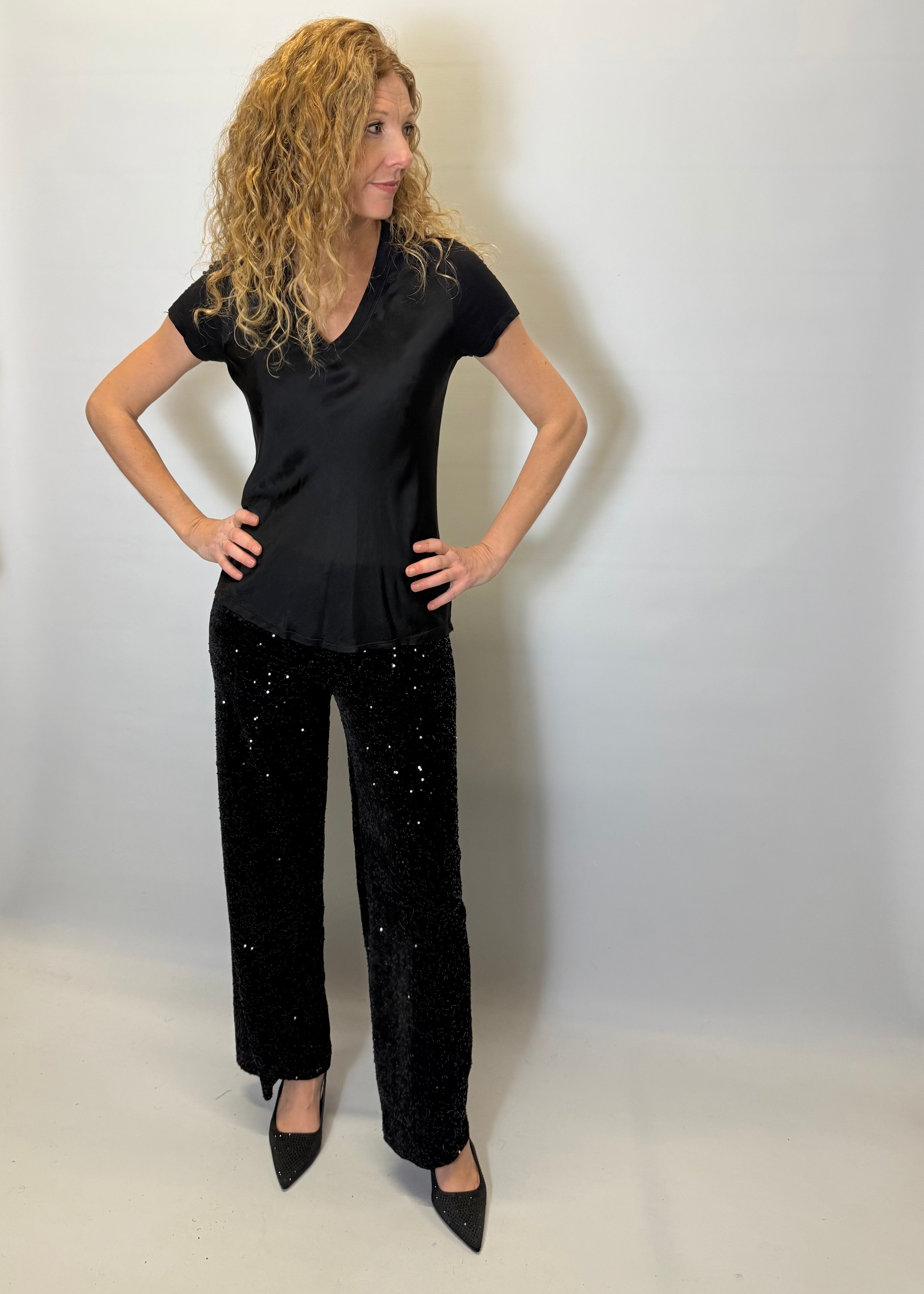 Woman wearing a black top and black pants with white speckles against a plain background