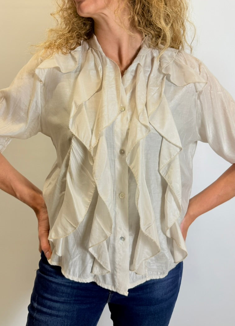 Woman wearing a white blouse with ruffled details against a neutral background