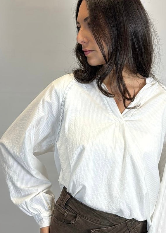 Woman wearing a white blouse with rolled-up sleeves against a plain background
