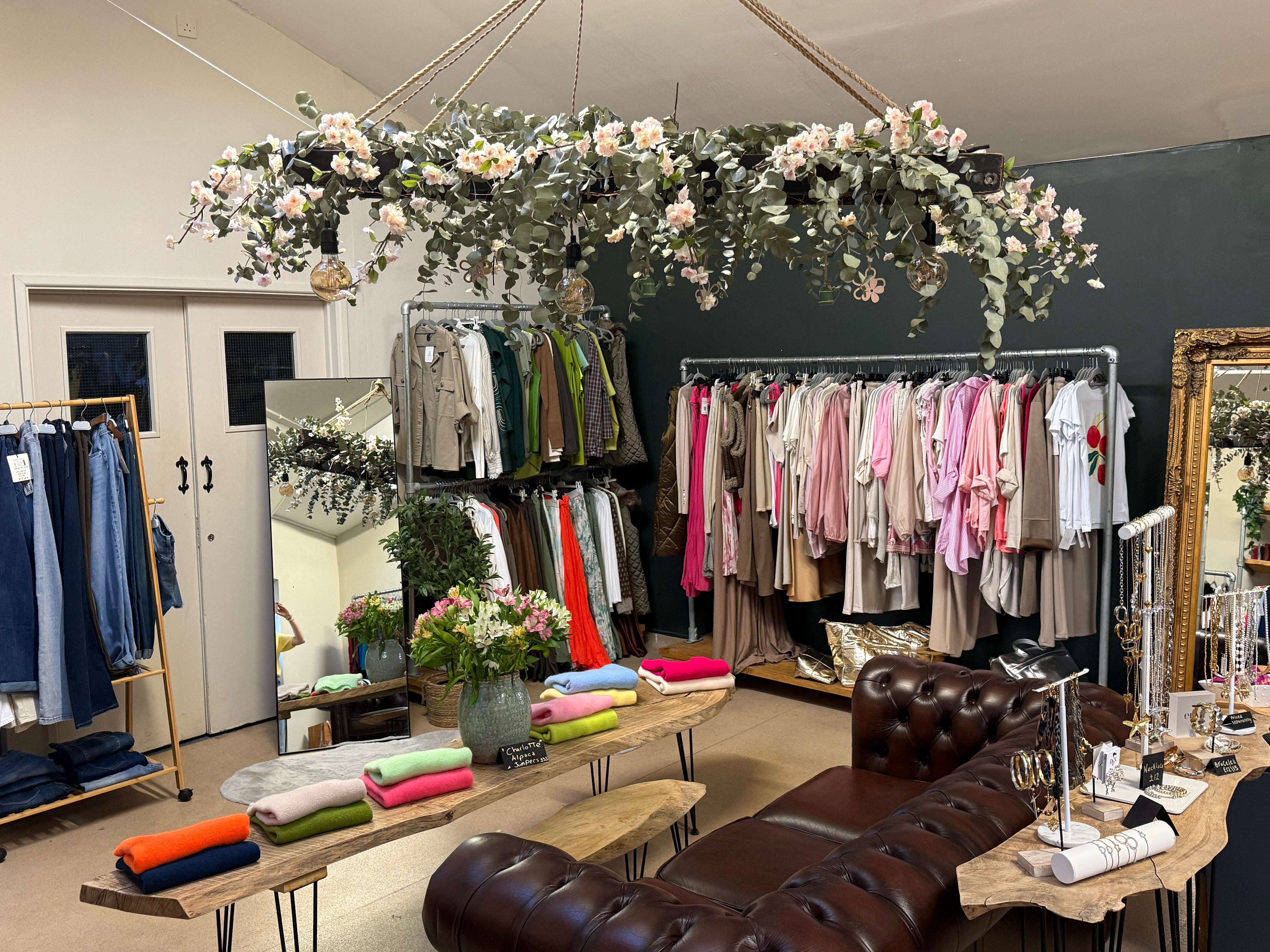 Clothing store interior with racks of clothes, a brown leather couch, and decorative elements.