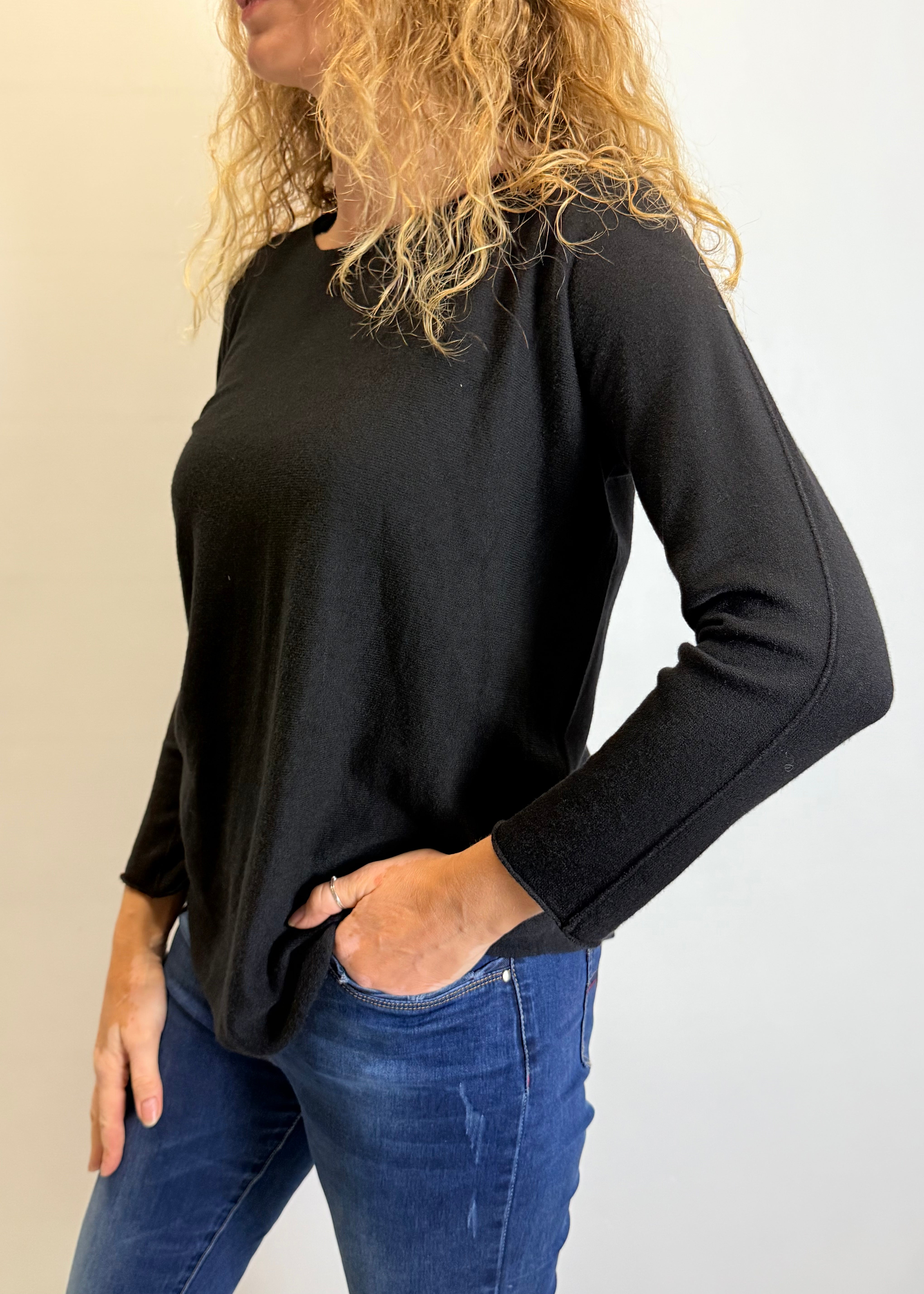 Woman wearing a black long-sleeve top and blue jeans against a plain background