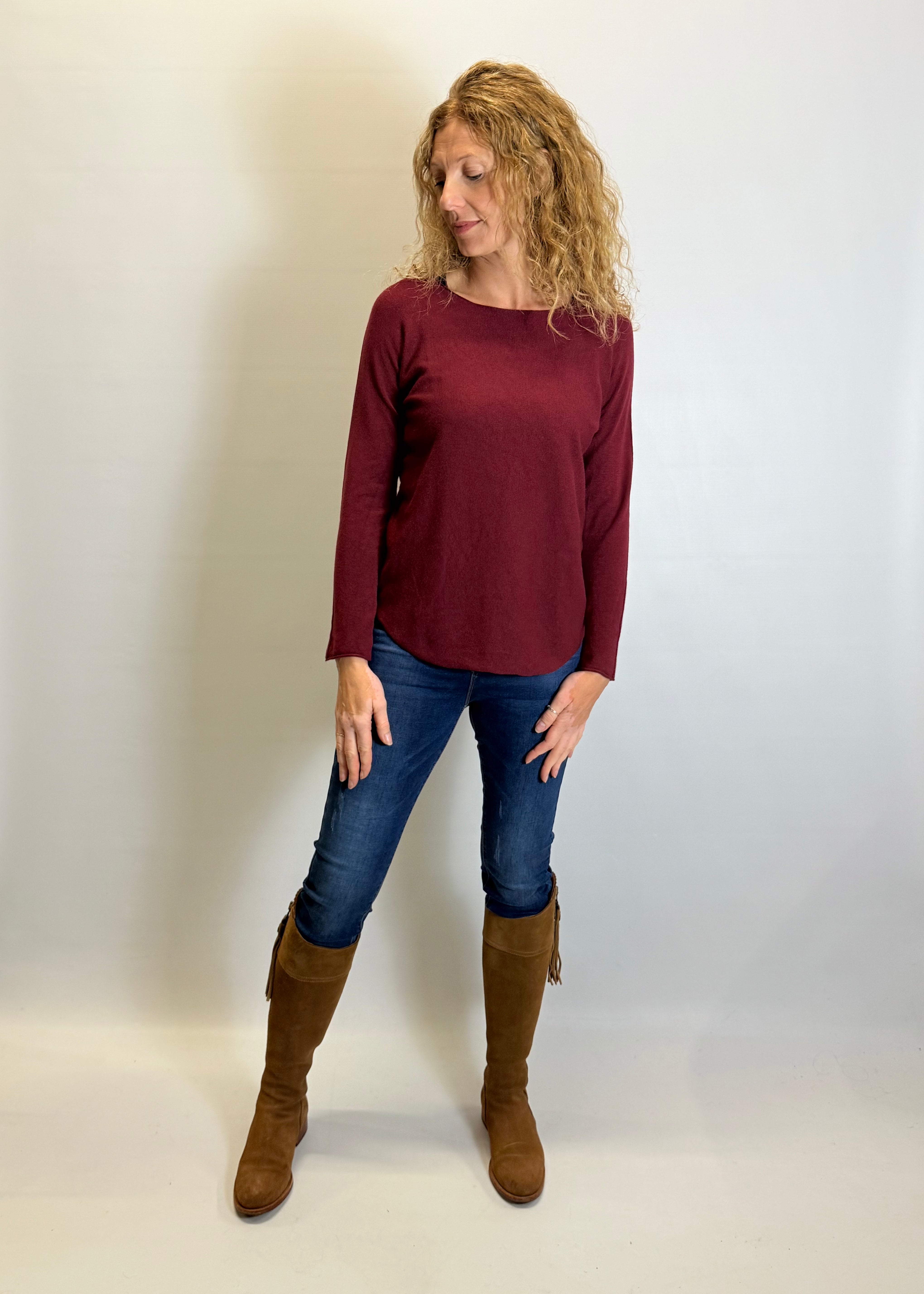 Woman wearing a burgundy sweater, blue jeans, and brown boots against a white background