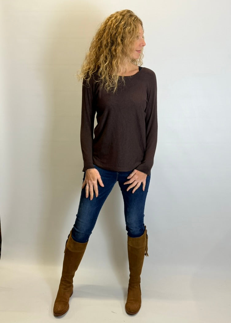 Woman wearing a brown long-sleeve top, blue jeans, and brown boots against a white background