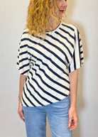 Person wearing a black and white striped shirt with blue jeans against a plain background
