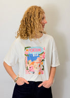 Person wearing a white t-shirt with a colorful graphic design on a plain background