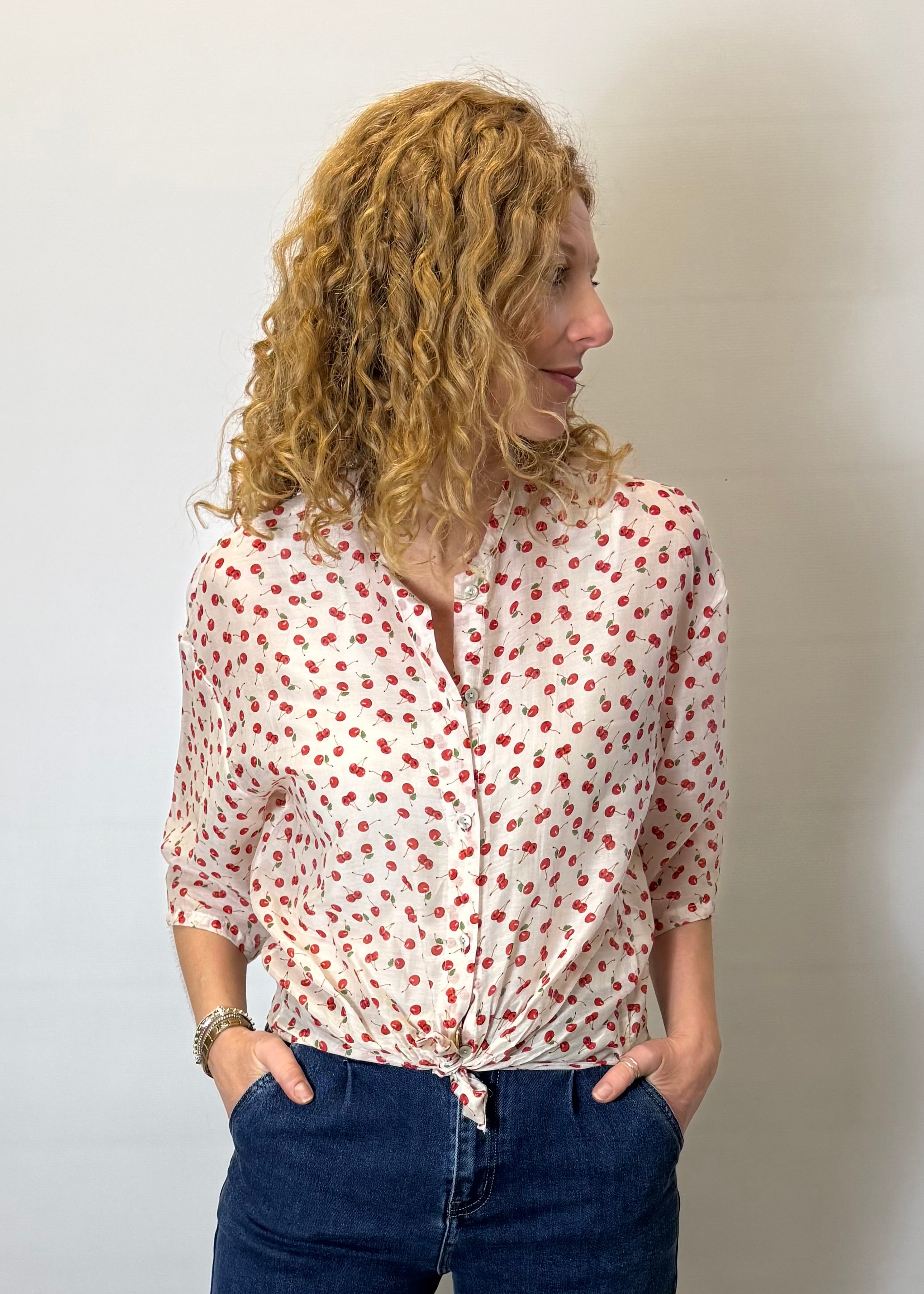 Woman wearing a white blouse with red patterns and blue jeans against a plain background