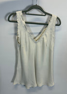 White top with lace trim on a hanger against a plain background