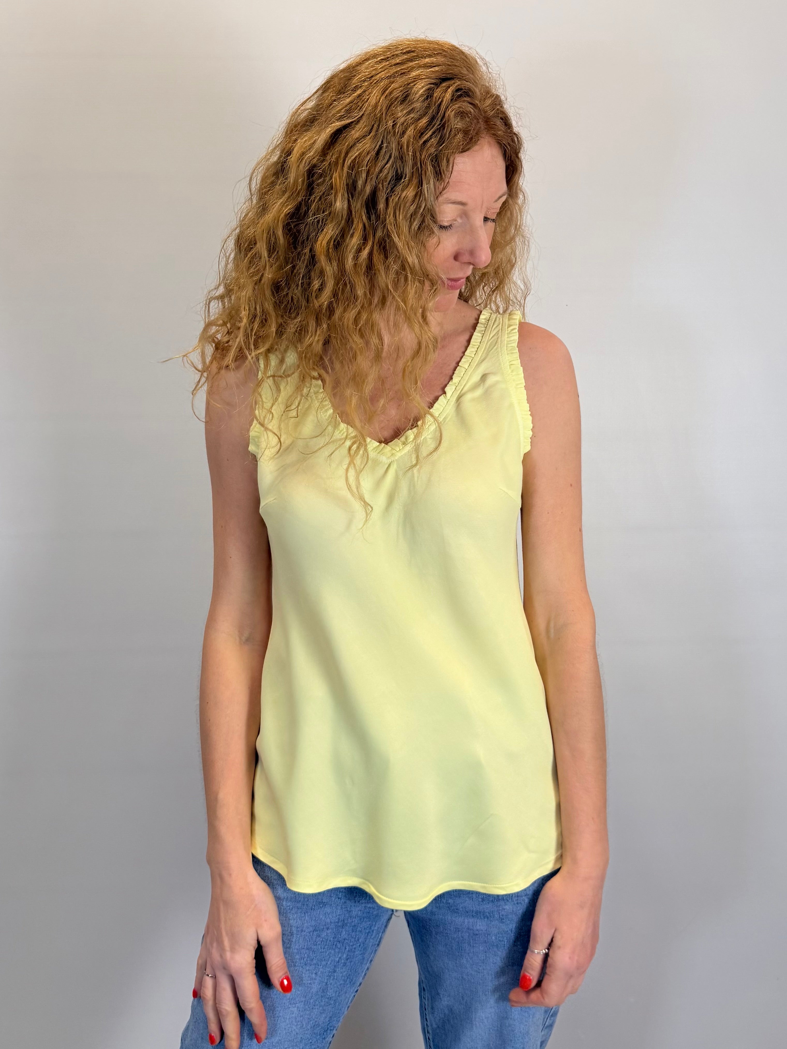 Woman wearing a yellow sleeveless top and blue jeans against a plain background