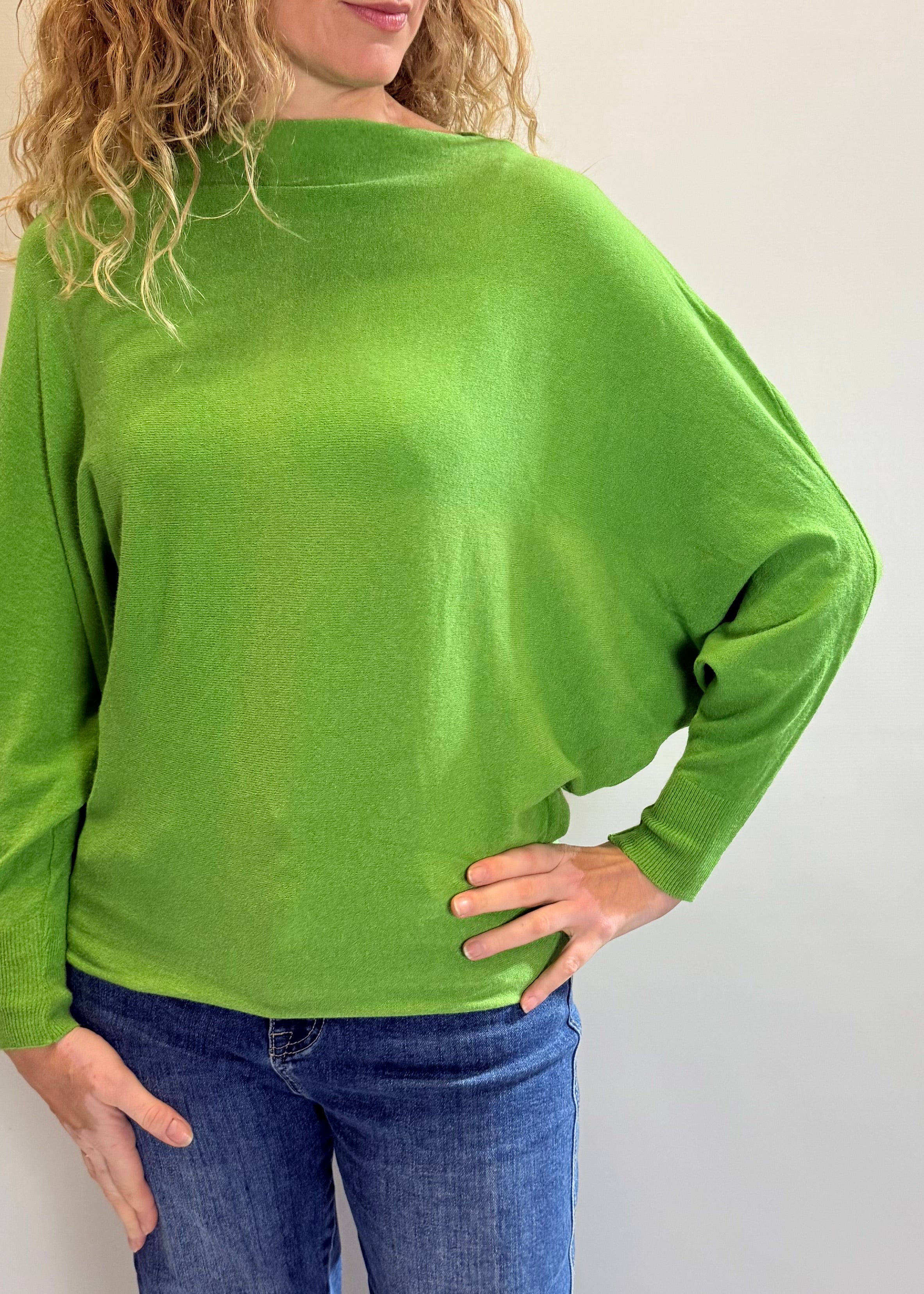 Person wearing a green long-sleeve top and blue jeans against a plain background