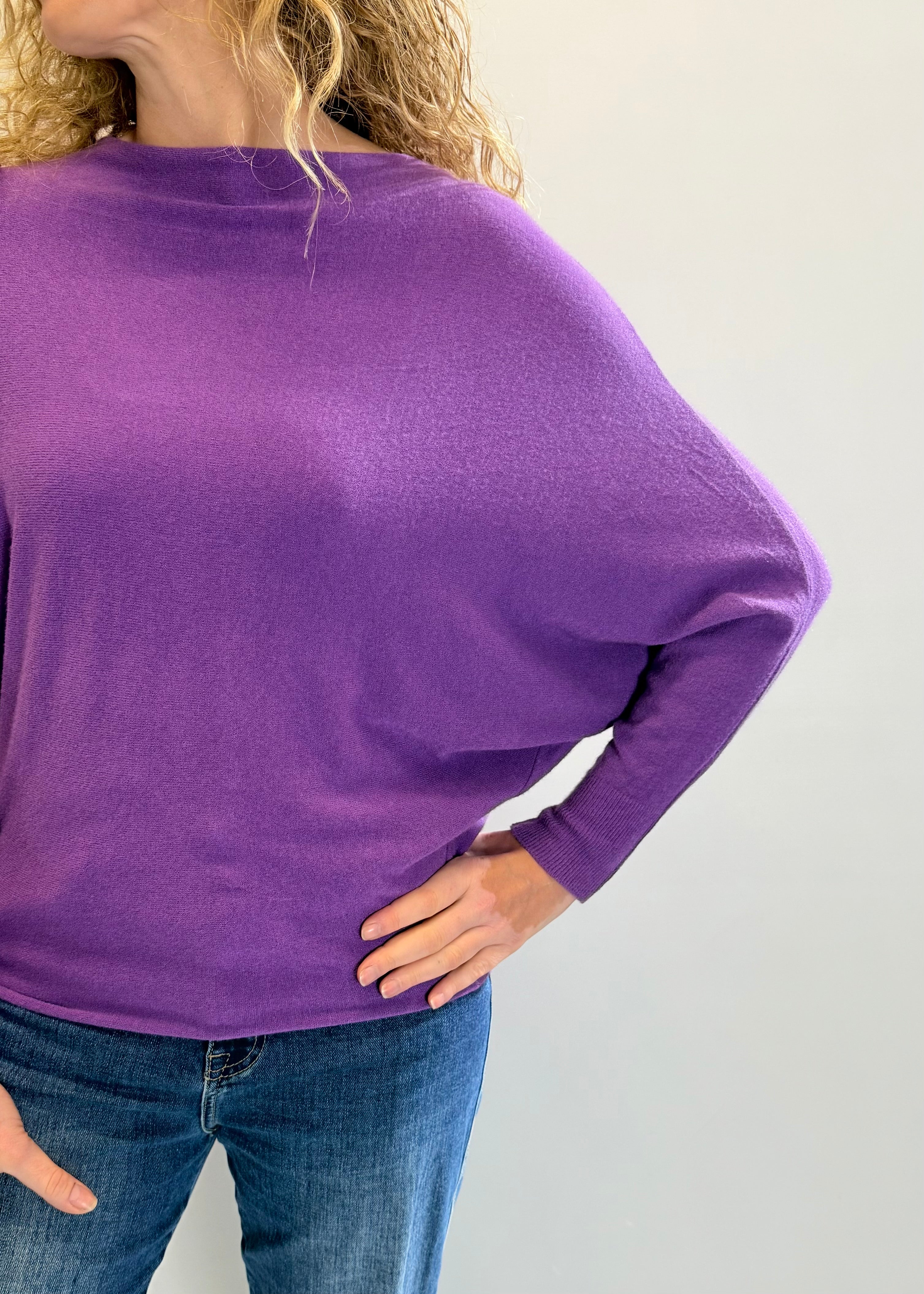 Person wearing a purple long-sleeve top and blue jeans on a plain background