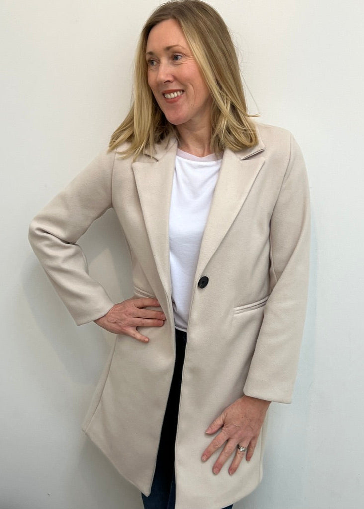A person wearing a burgundy blazer over a white top, paired with blue jeans and brown boots, standing in a room with a leather ottoman.