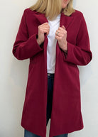 Person wearing a burgundy coat over a white shirt and blue jeans against a plain background