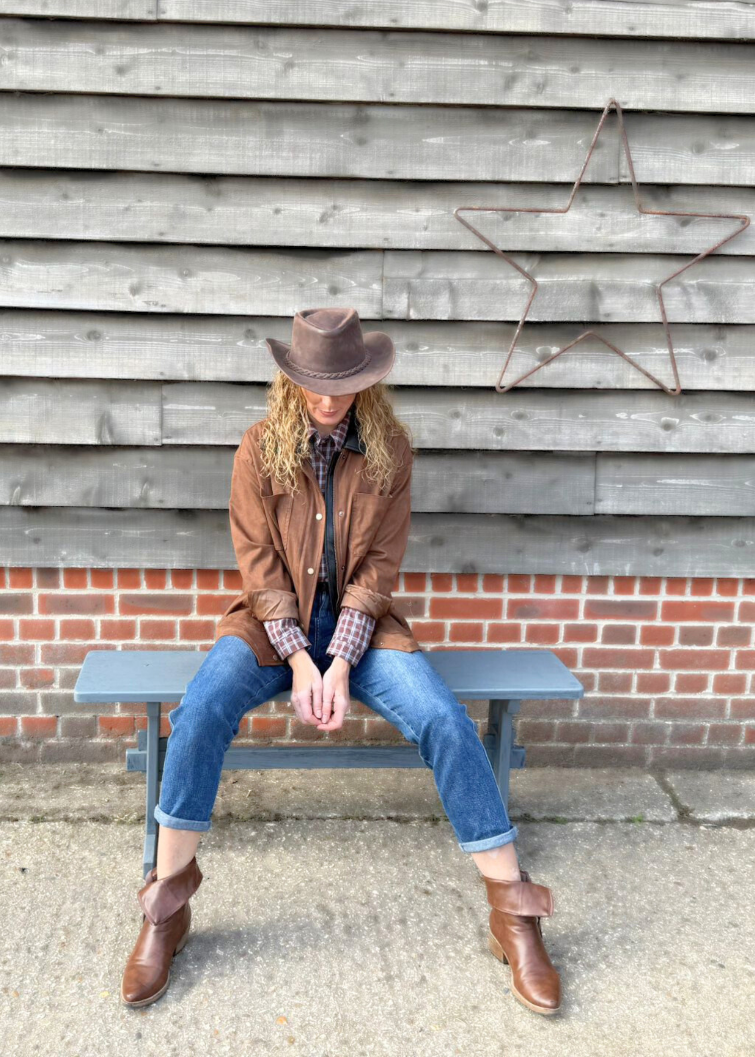 Woman wearing country style clothes with brown jacket, check shirt and jeans available in ladies shop near Basingstoke in Hampshire.