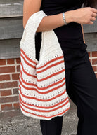 Person holding a white and red striped bag against a brick wall.