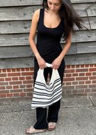 Woman holding a striped bag against a wooden wall.