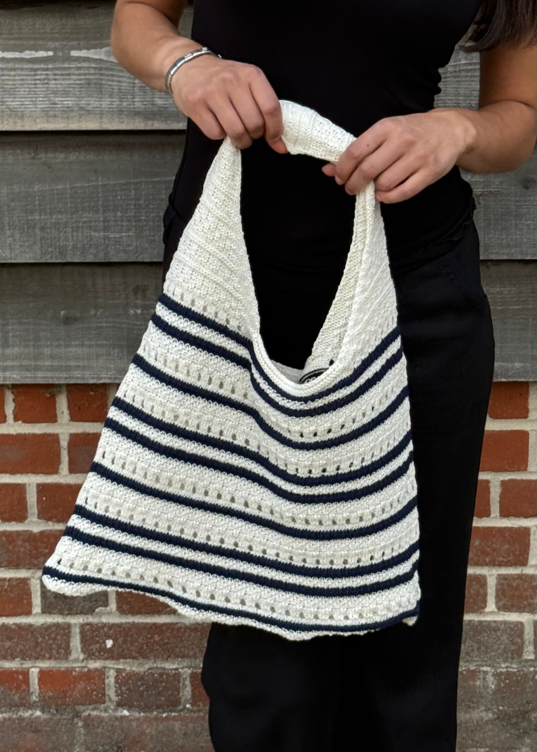 Person holding a striped crochet bag against a brick wall.