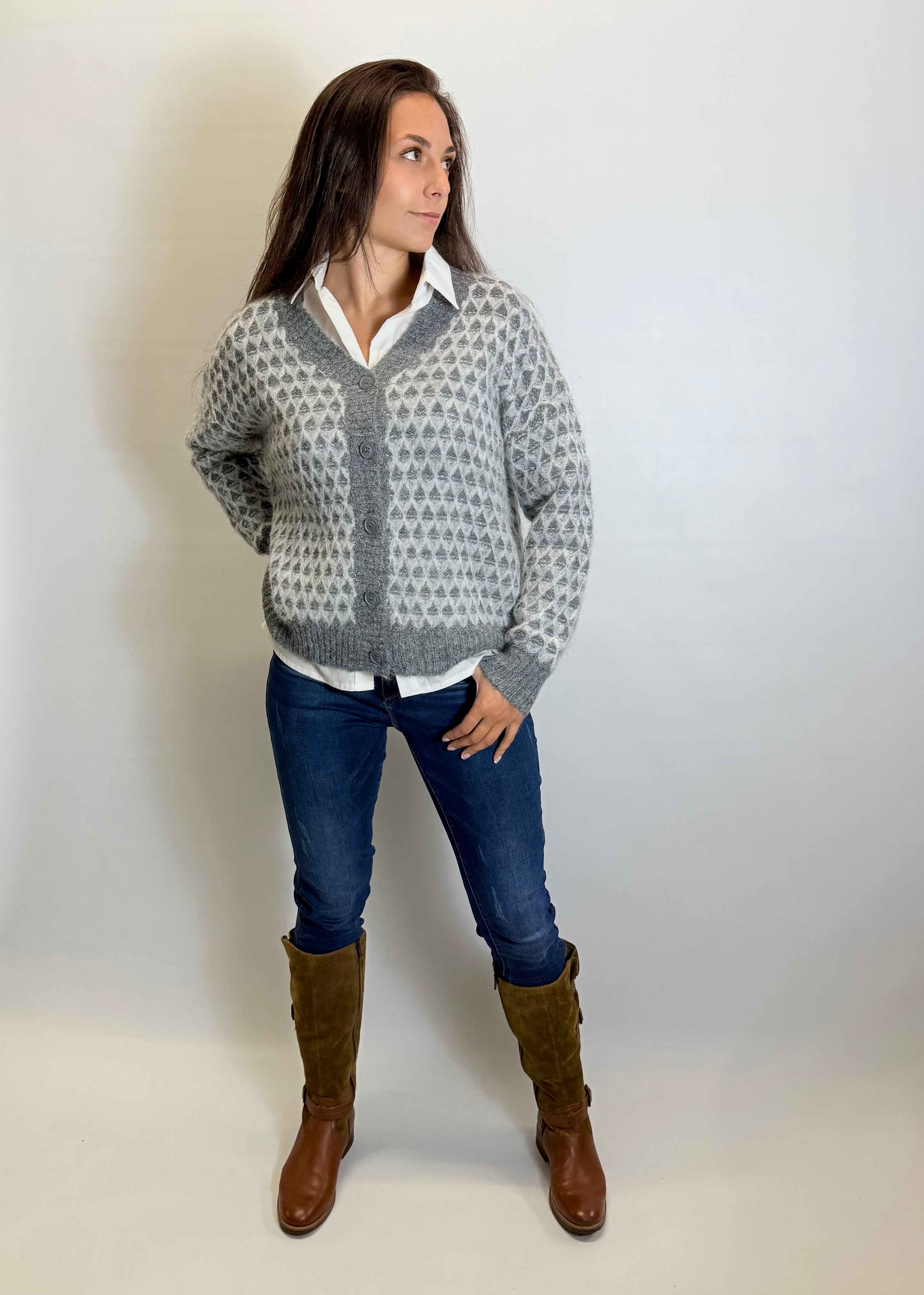 Woman wearing a patterned sweater, white shirt, blue jeans, and brown boots against a plain background