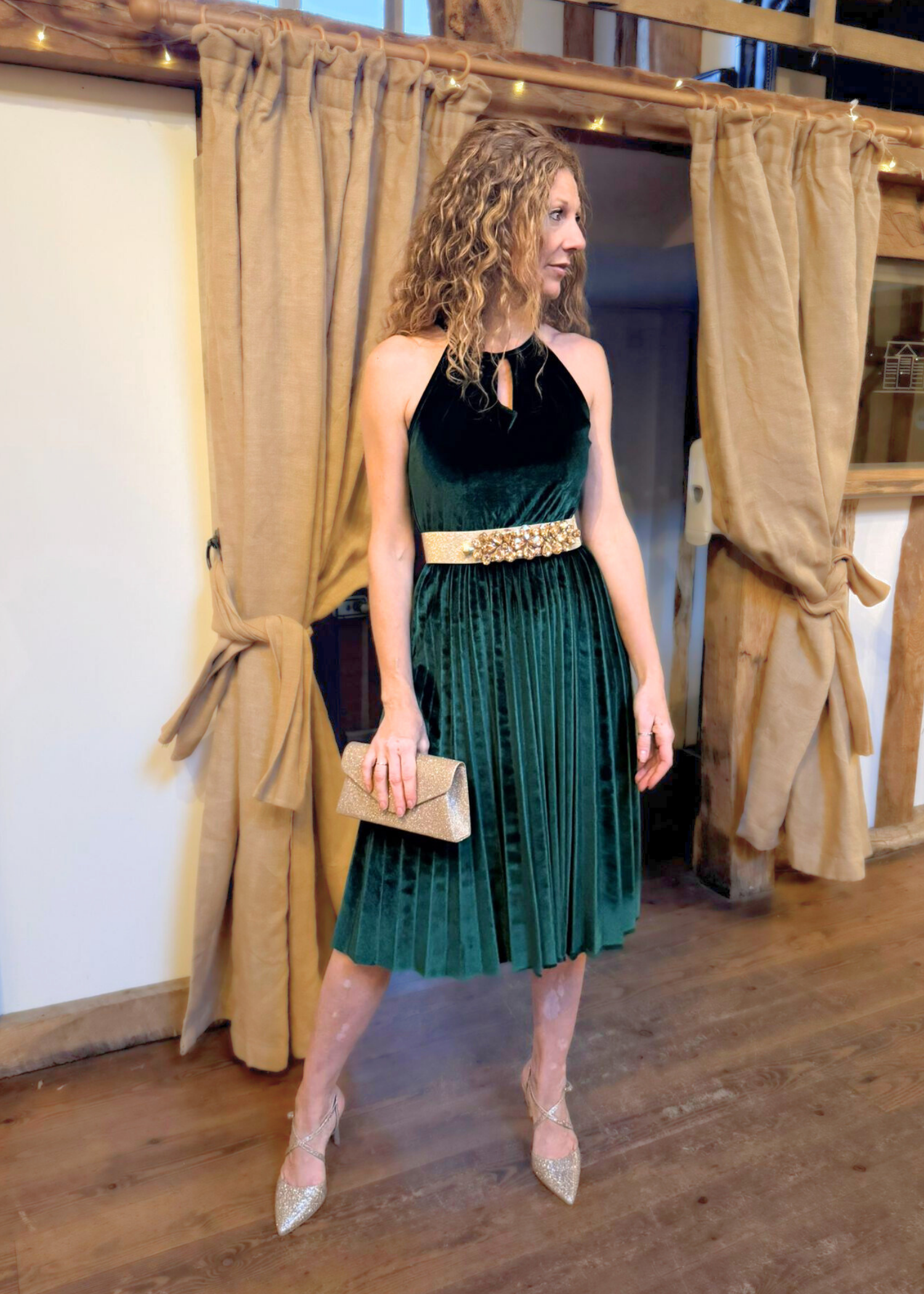 Lady wearing green velvet dress with gold belt and gold clutch bag.