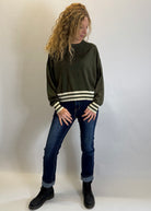 Woman wearing a green sweater with white stripes and blue jeans against a plain background