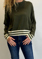 Person wearing an olive green sweater with striped cuffs on a plain background