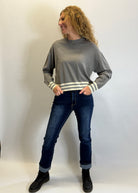 Woman wearing a gray sweater with white stripes and dark jeans against a plain background