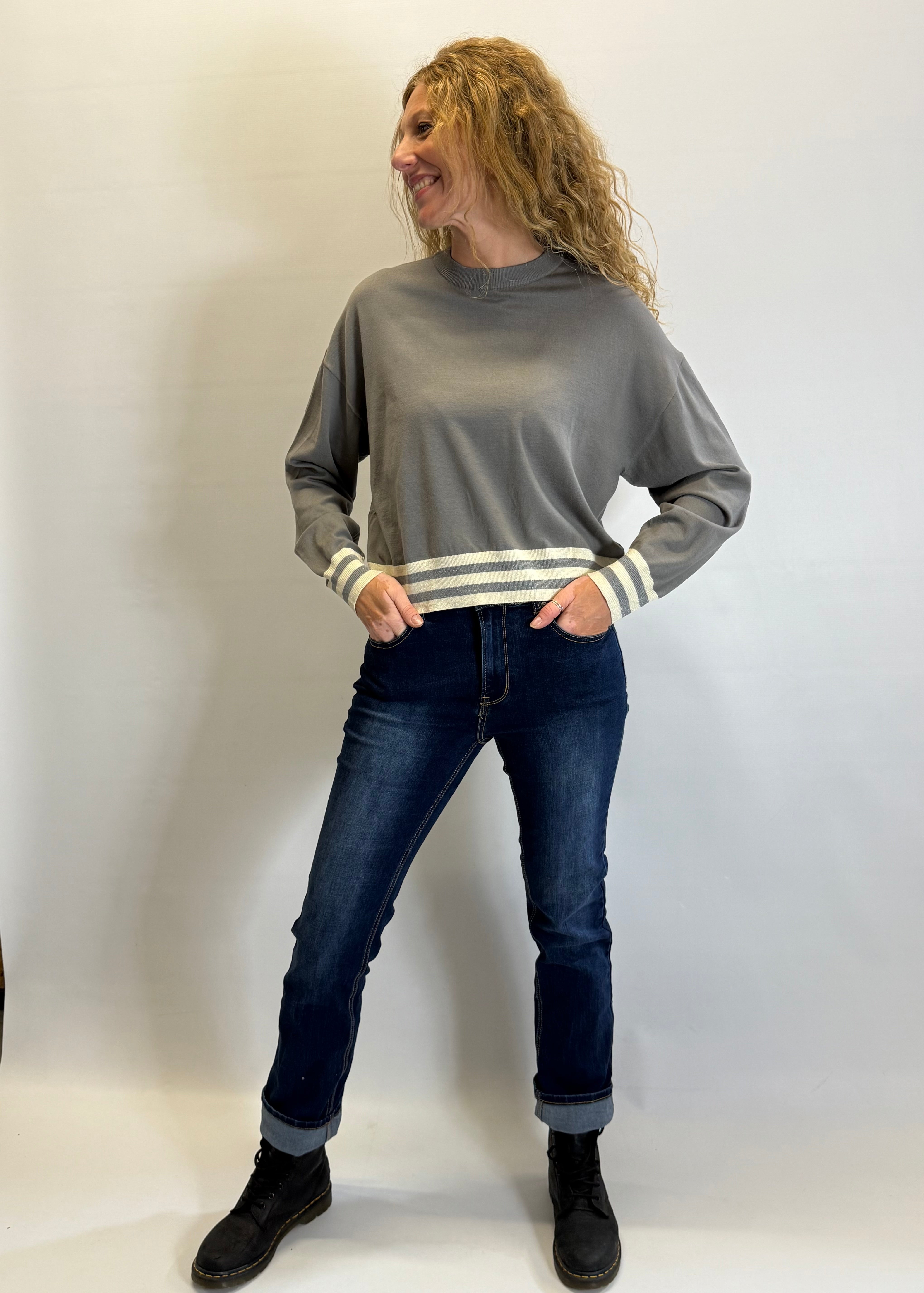 Woman wearing a gray sweater with white stripes and dark jeans against a plain background
