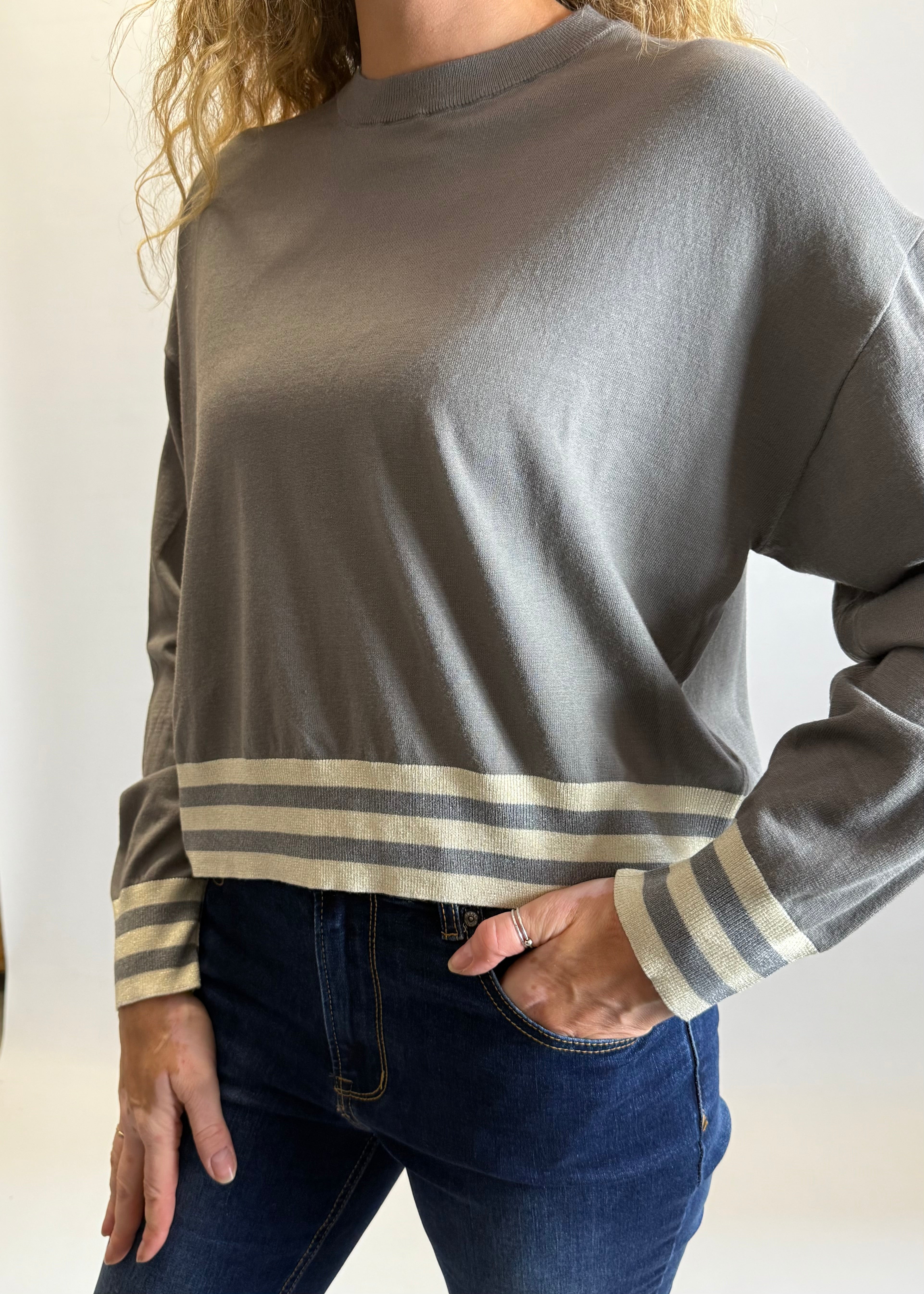Person wearing a gray long-sleeve shirt with striped cuffs against a neutral background